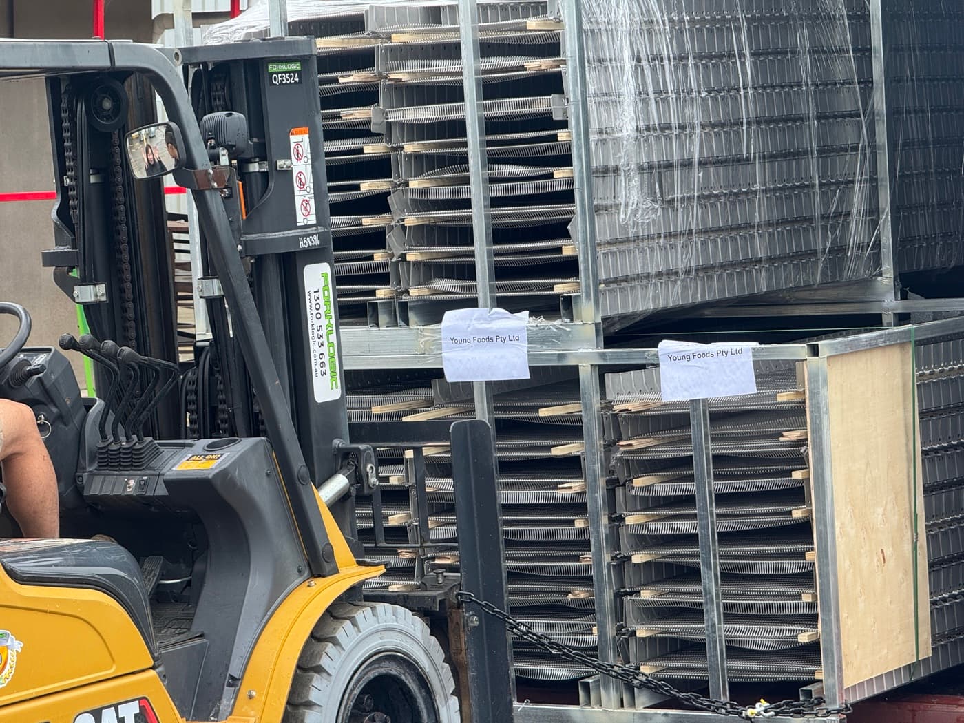 A forklift unloading steel crates of conveyor equipment labelled Young Foods Pty Ltd